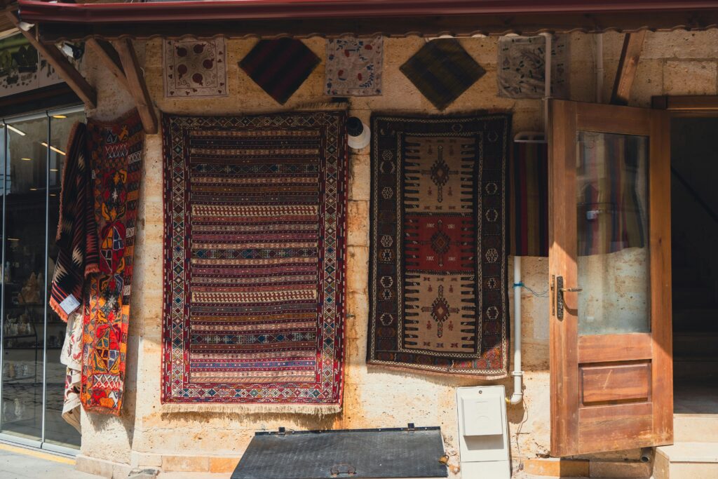 Handmade carpets hanging on an outdoor wall beside an open wooden door. A showcase of traditional craftsmanship.