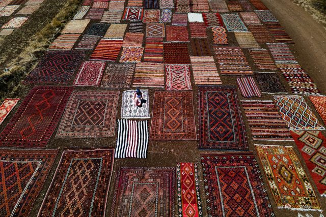 Vibrant Turkish rugs on display outdoors in a rural setting, viewed from above.
